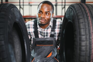 Car tire service concept. Portrait African american man mechanic holding new tyre on background...