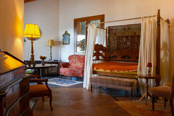 Open-space interior finely decorated with classical-style furniture, with a four-poster bed and a red armchair under a window