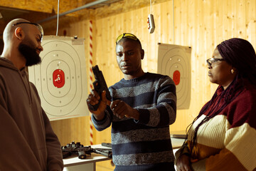 Shooting range safety officer teaching students how to cock pistol before firing. Firing range instructor providing comprehensive framework to achieve high level of proficiency with weapons