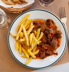 Appetizing chicken gizzards cooked in vegetables salsa with side dish of fried potatoes