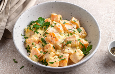 Bowl of pumpkin in sour cream sauce sprinkled with fresh parsley on beige textured stone table. Vegetarian food