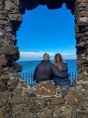 Couple sitting on old ruins, looking out over the ocean