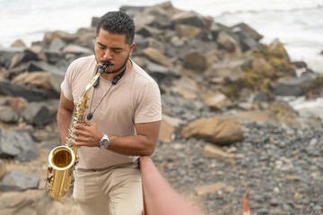 Musician playing saxophone seeking inspiration on rocky beach