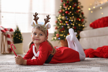 Little girl in Christmas costume with candy cane lying on floor at home