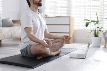 Man meditating near laptop on floor at home, closeup