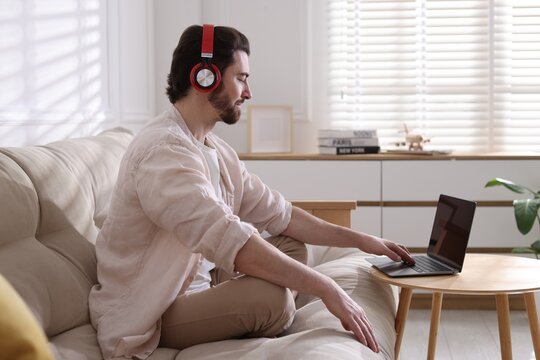 Meditation. Man in headphones watching video tutorial by laptop on sofa at home