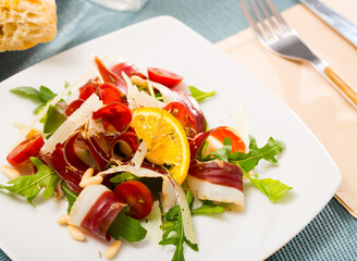 Colorful salad from duck ham with fresh arugula, tomatoes, sliced parmesan cheese, pine nuts and orange