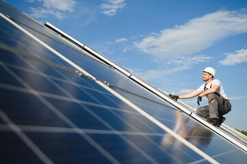 Side view of male worker installing solar modules and support structures of photovoltaic solar...