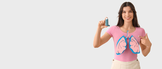 Young woman with asthma inhaler pointing at paper lungs on white background