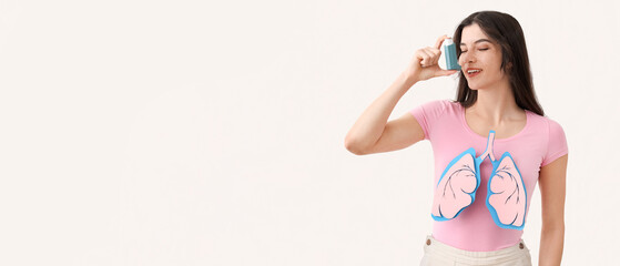 Young woman with paper lungs and asthma inhaler on white background