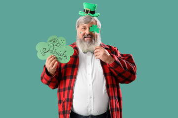 Mature man with card and paper clover on green background. St. Patrick's Day celebration