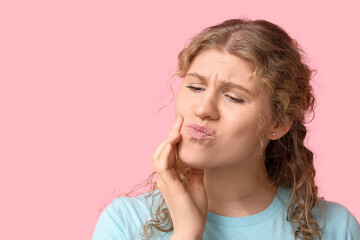 Beautiful young woman suffering from toothache on pink background