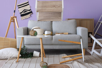 Interior of messy living room with grey sofa and overturned furniture after earthquake