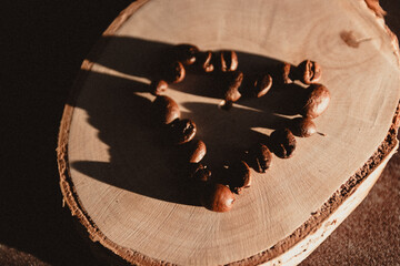 Coffee beans arranged in a heart shape on a wooden slice in warm, contrasting lighting - shot from above, horizontal orientation