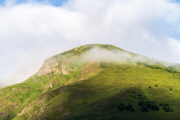 Green mountain slope with soft morning fog and sunlight under blue sky. Travel nature and eco...