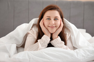 Beautiful young woman lying under blanket in bed at morning