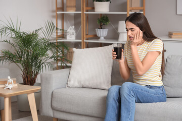 Young woman suffering from toothache with soda on sofa at home