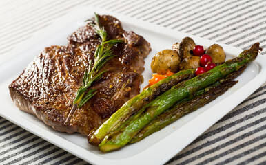 Roasted veal steak with seasonings served with baked vegetables and rosemary on striped textile surface