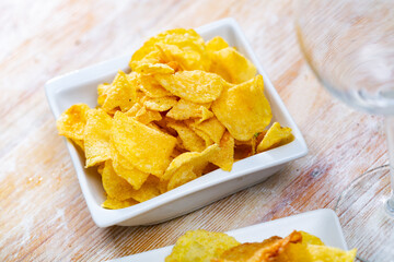 Crispy potato chips in white square ceramic plate on rustic wooden table