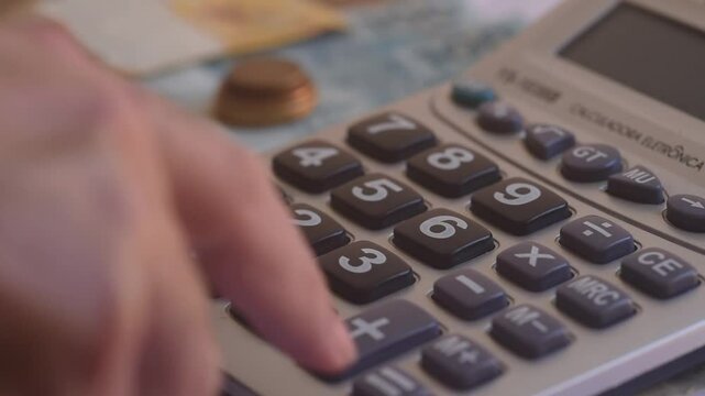 Men hand typing on calculator button to calculate for personal tax or expense budget on the wooden table inside of the house with blurred paper note and pen. Financial and money saving concept.
