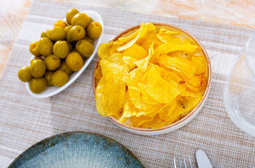 Crispy chips and large green olives served as snack in bowl