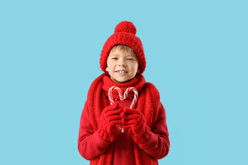 Cute fashionable boy in warm red sweater, scarf and winter hat with candy canes on blue background