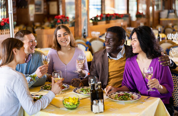 Group of joyous friends enjoying evening meal at cozy restaurant