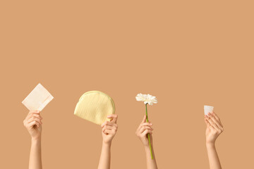 Many female hands with menstrual cup, pad and cosmetic bag on beige background