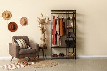 Armchair, rack with clothes and accessories in interior of hallway