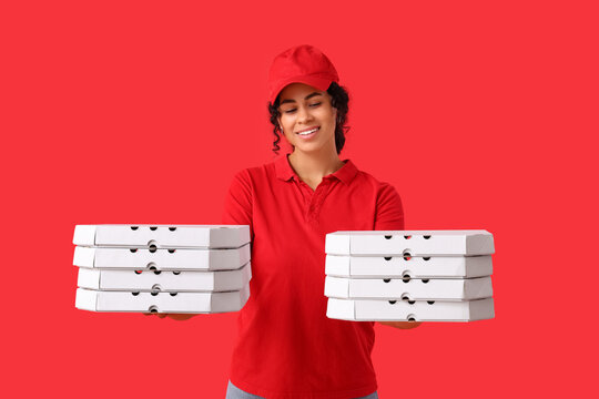 Female African-American courier holding cardboard boxes with tasty pizza on red background