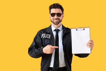 Happy male police officer pointing at clipboard on yellow background