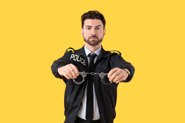Male police officer with handcuffs on yellow background