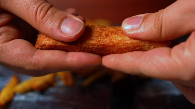 Hands breaking up crispy yuca with French fries in the background