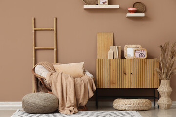 Interior of living room with wicker armchair, ladder and home decor on commode
