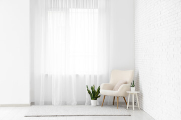 Armchair with table and plants on carpet near light curtain in room