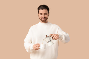Young man with geyser coffee maker and cup on beige background