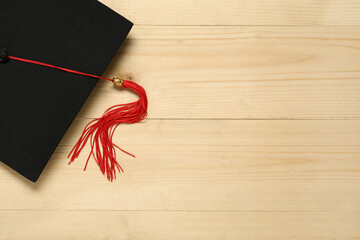 Graduation hat on wooden background, top view