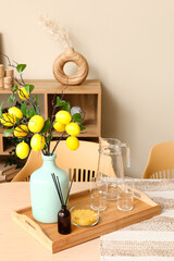Vase with lemon tree branches, jug and glasses on dining table in room