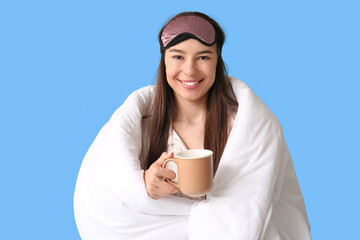 Young woman with coffee cup and blanket on blue background