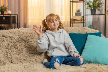 Young teenager girl waving hand with happy smile at home, expressing joy and friendliness....