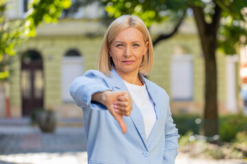 Sad upset disappointed Caucasian mature businesswoman female woman in formal suit showing thumb...