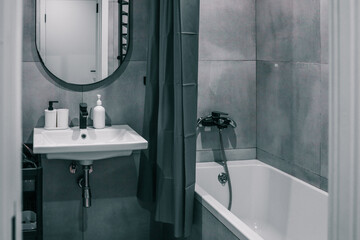 Modern bathroom with minimalistic design, featuring a white sink, wall-mounted mirror, gray shower...