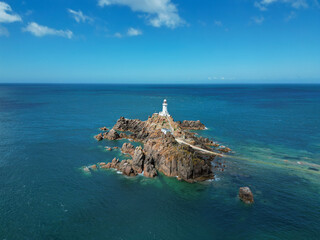 Scenic aerial drone view of La Corbiere lighthouse on a rocky island surrounded by turquoise water. Jersey, Channel Islands