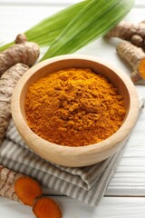 Aromatic turmeric powder, fresh roots and leaves on white wooden table, closeup