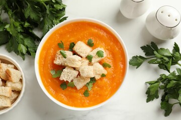 Delicious pumpkin cream soup with croutons, parsley and ingredients on white table, flat lay