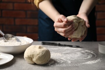 Woman kneading raw dough at light grey table, closeup