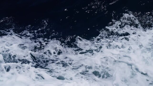 Foamy seawater swirling across dark oceanic surface, generating intricate white patterns, revealing fluid maritime textures and rhythmic aquatic movement
