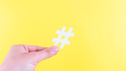 Hand holding a white hashtag symbol against bright yellow background for social media marketing