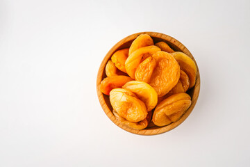 Wooden bowl filled with dried apricots on a clean white background, showcasing their vibrant orange color and natural wrinkled texture