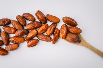 Flat lay of dried dates artfully arranged in a leaf shape with a wooden spoon as the stem on a white background. Creative organic food concept for healthy lifestyle or packaging design